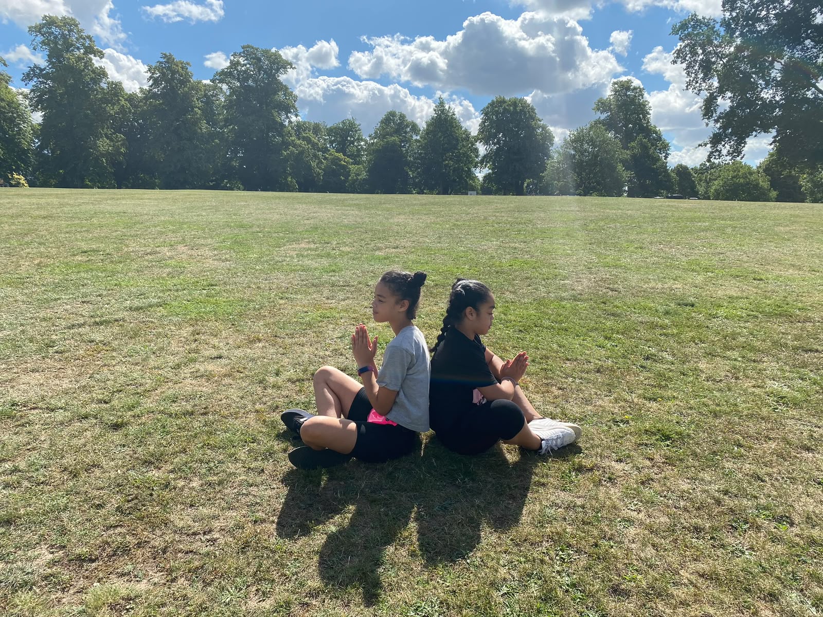Children sitting back to back outdoors during yoga practice